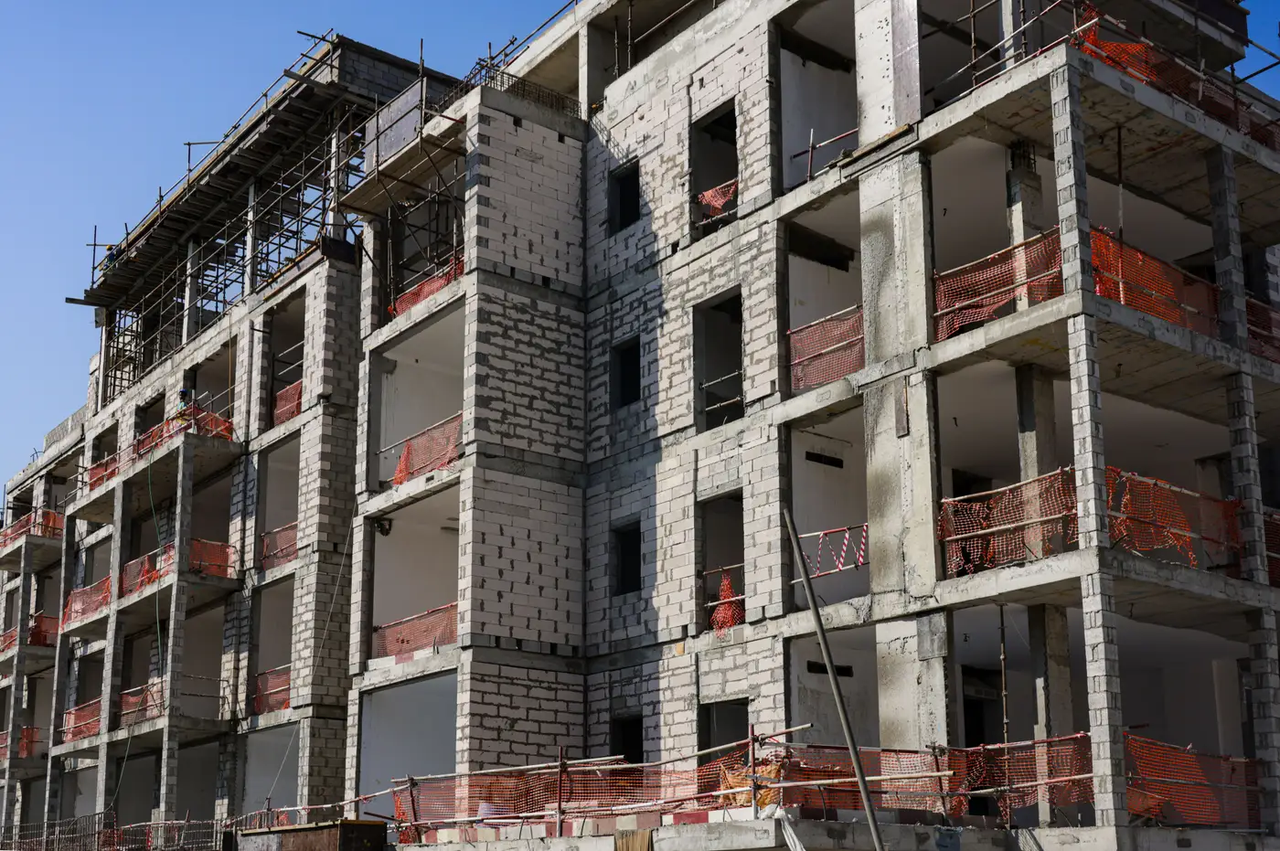 A multi-story concrete apartment building under construction with scaffolding and safety netting.